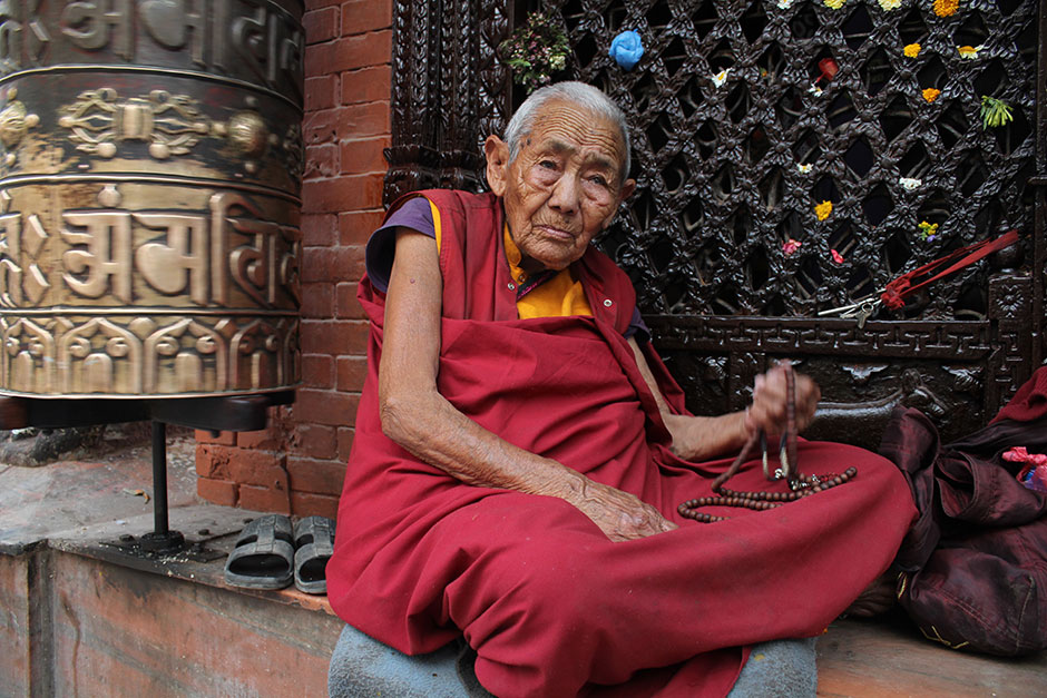 a buddhist devotee sitting besides prayer wheet in temple 