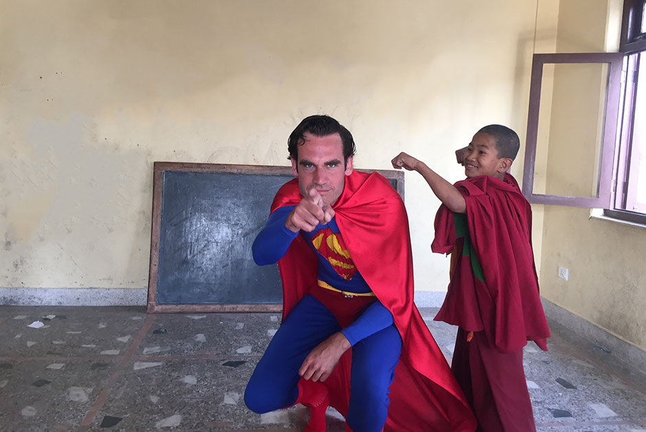 lammert pointing finger to the camera as superman and monk kid in backdrop
